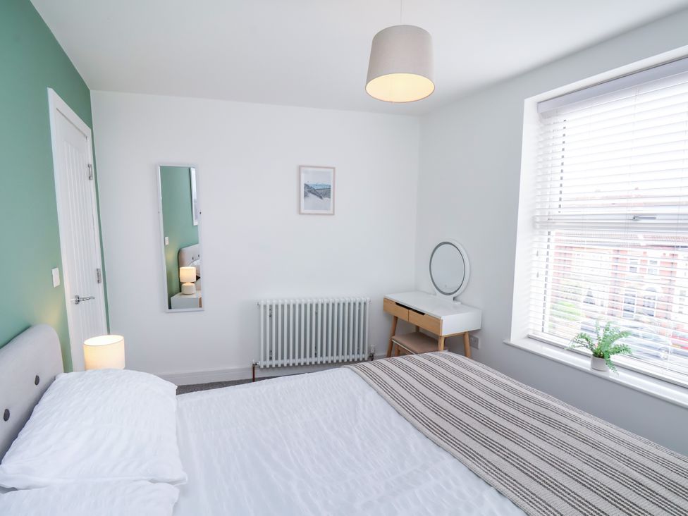 A bedroom with a bed, lamp, mirror, radiator, and dresser at Apartment 6 (1 bed) Redcar