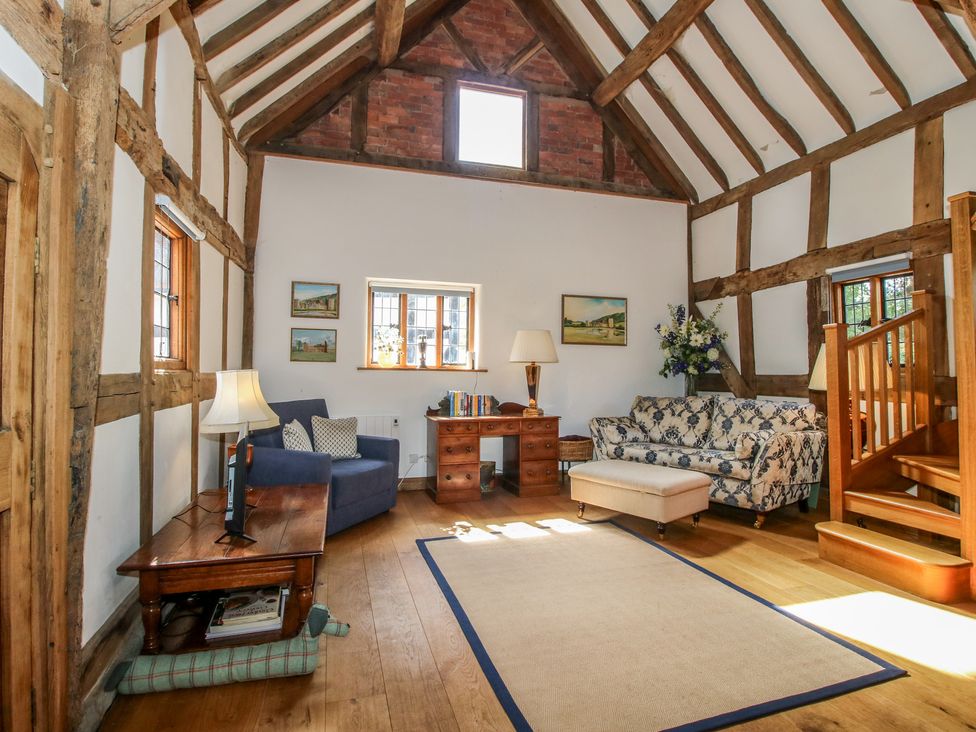 A living room with a sofa and wooden staircase at Courtyard Cottage in Little Stretton