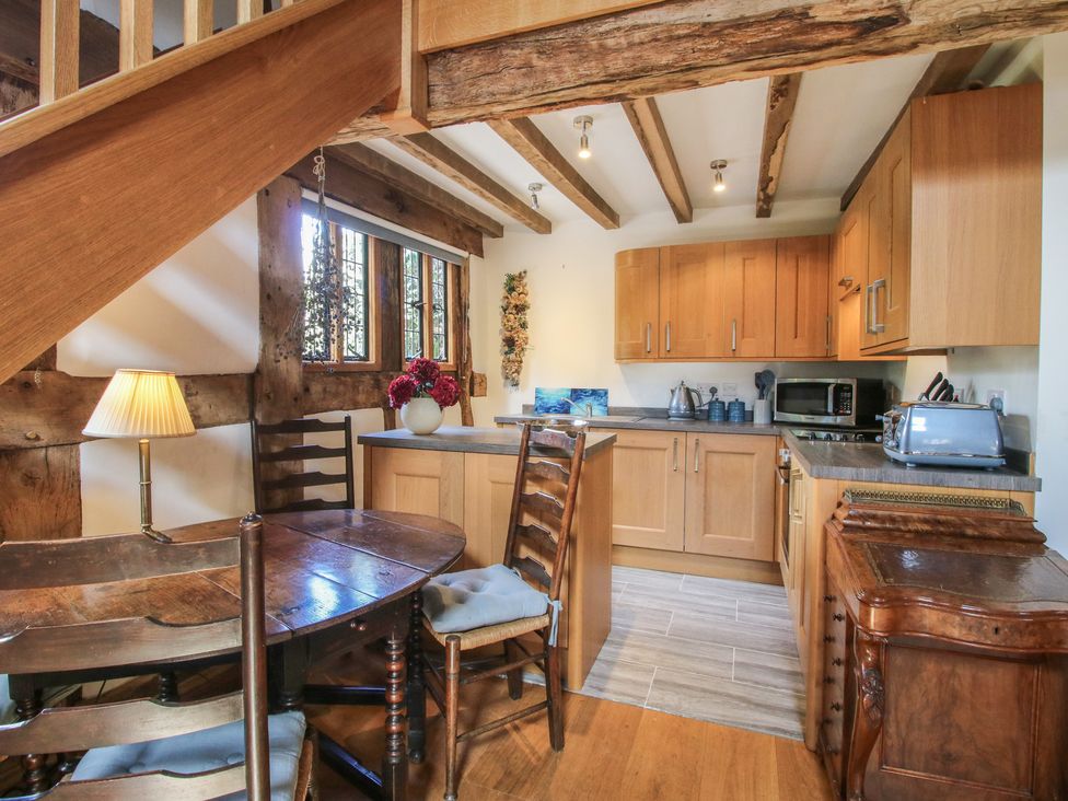 A kitchen with wooden cabinets and a dining table at Courtyard Cottage in Little Stretton