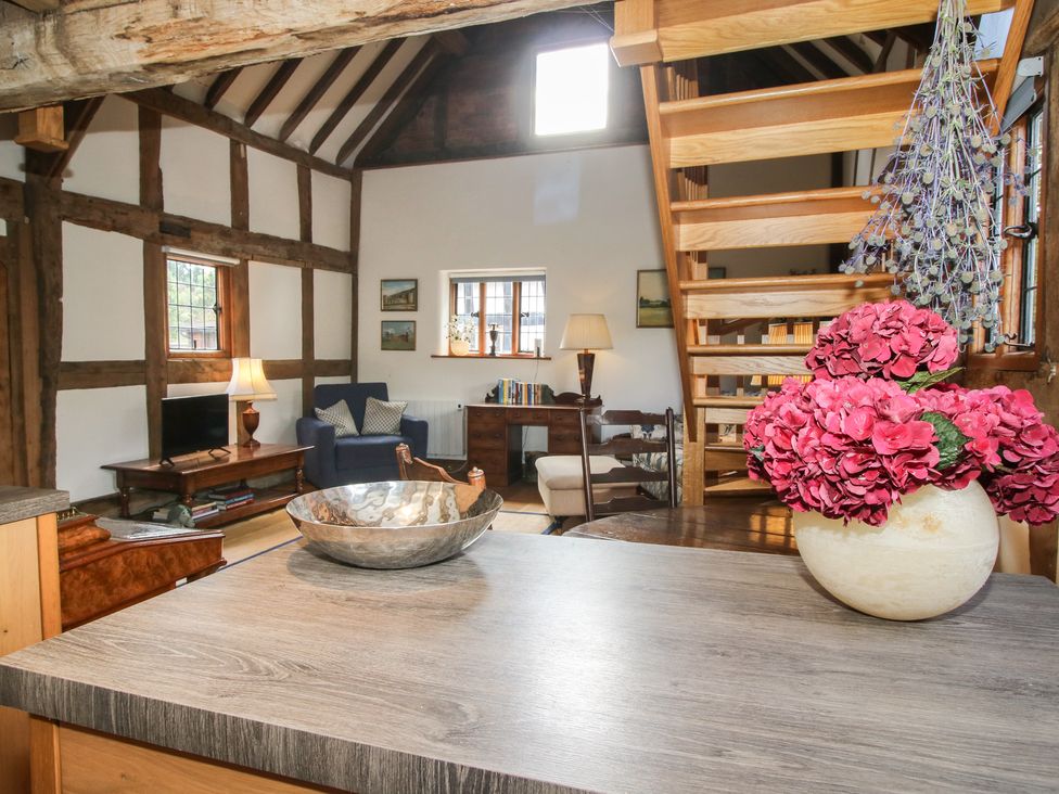 A living room with a staircase and a flower arrangement at Courtyard Cottage in Little Stretton