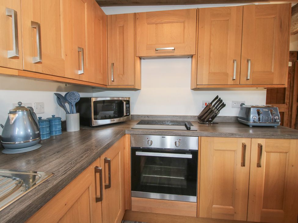 A kitchen with wooden cabinets and appliances at Courtyard Cottage in Little Stretton