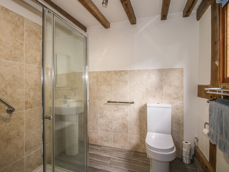 A bathroom featuring a shower, toilet, and sink at Courtyard Cottage in Little Stretton