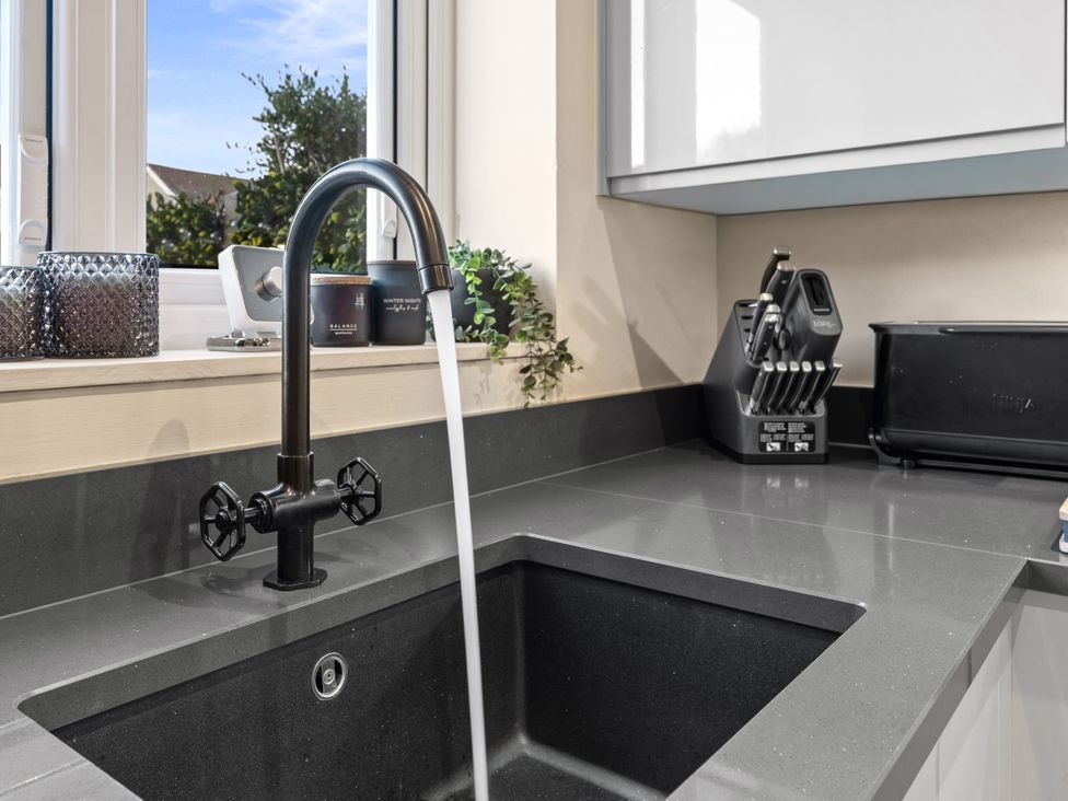A kitchen sink with a faucet and storage items at Hafan Rhos in Rhos-On-Sea