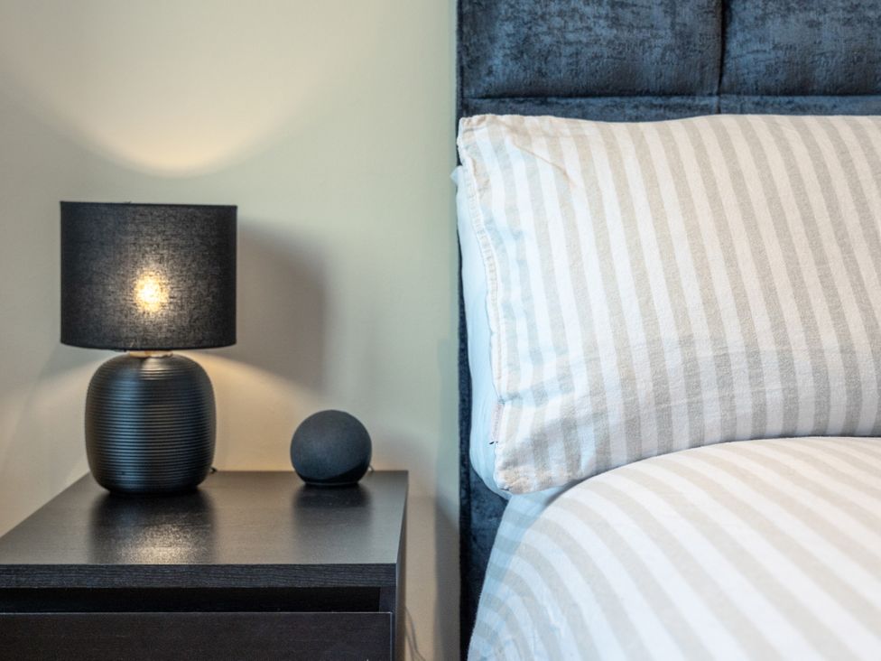 A bedside table with a lamp and smart speaker next to a bed at Hafan Rhos Rhos-On-Sea