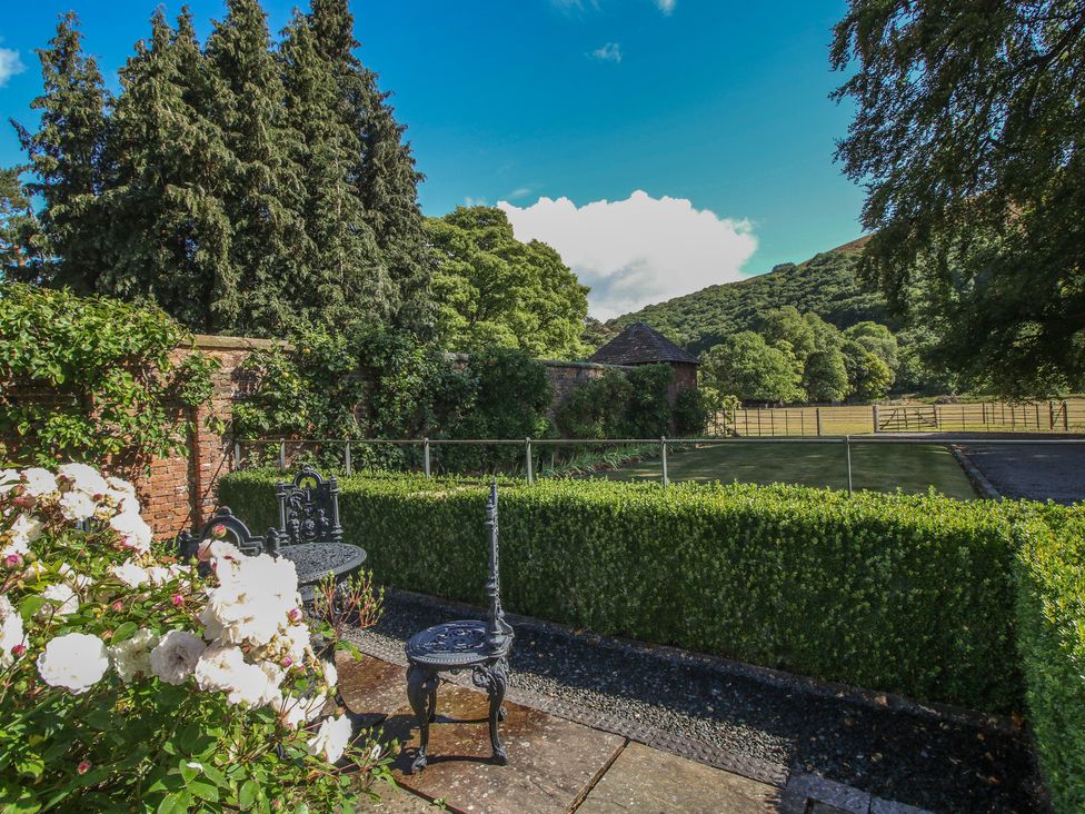 A garden with a stone pathway, hedge, table and chair at The Coach House in Little Stretton