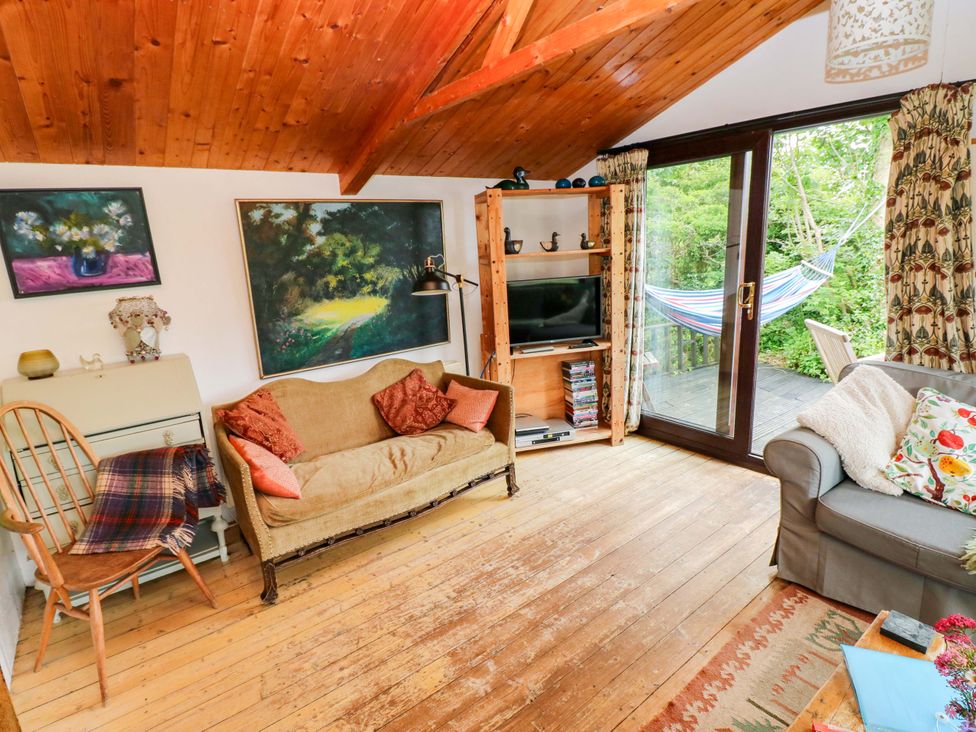 A living room with a sofa, armchair, and TV at The Tree House in Nine Wells near Solva