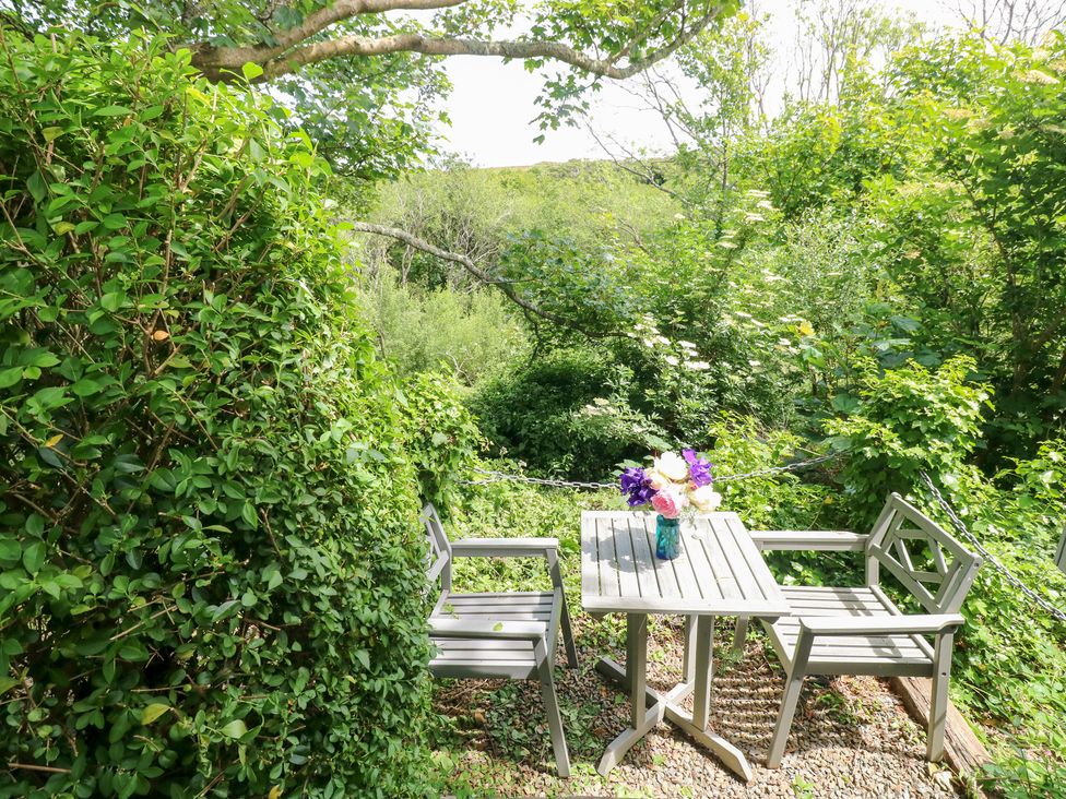 A garden area with a table and chairs surrounded by greenery at The Shephard Hut, Nine Wells near Solva