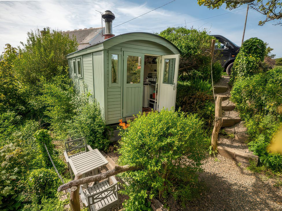 A hut surrounded by greenery with steps leading to a driveway at The Shepherd Hut near Nine Wells near Solva