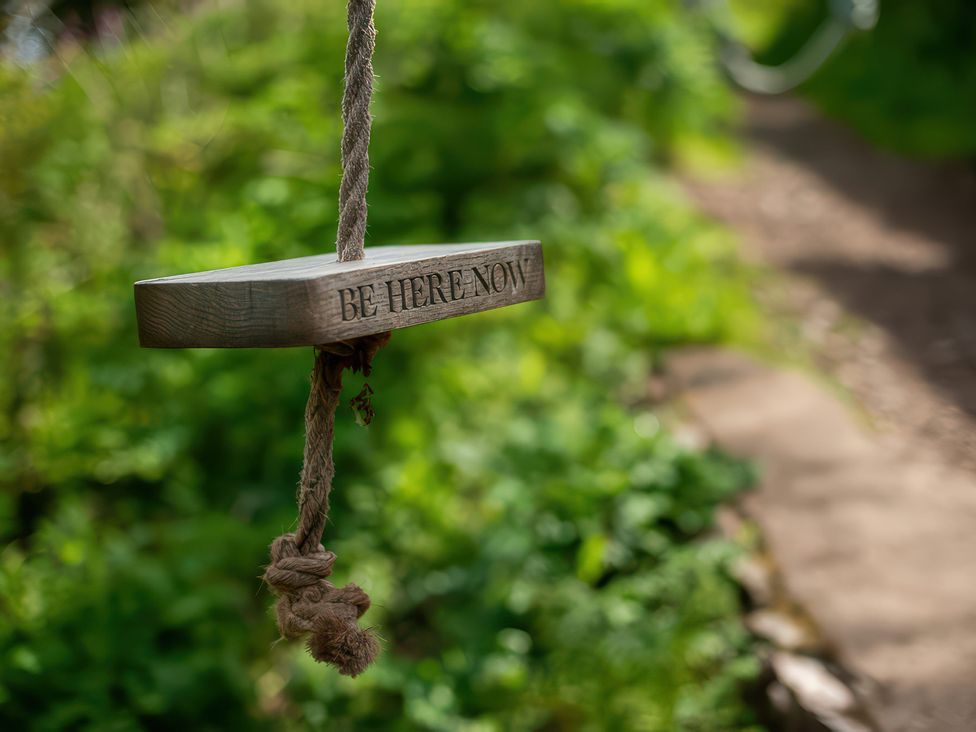 A wooden sign hanging on a rope in a garden area at The Shepherd Hut, Nine Wells near Solva