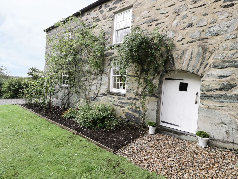An outdoor area with a stone wall, plants, and a door at Bwthyn Canol in Llanfair