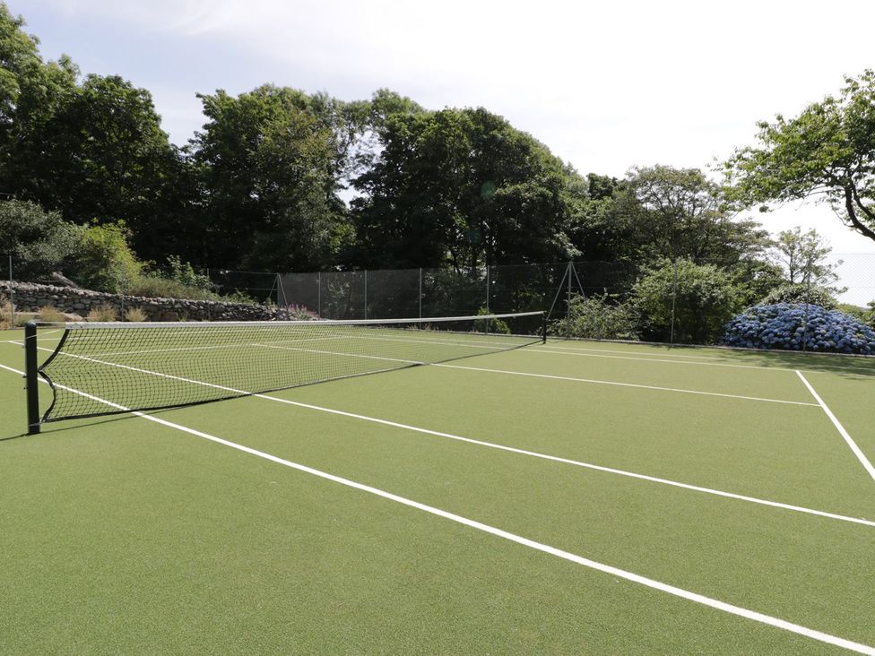A tennis court with net and greenery at Bwthyn Canol in Llanfair