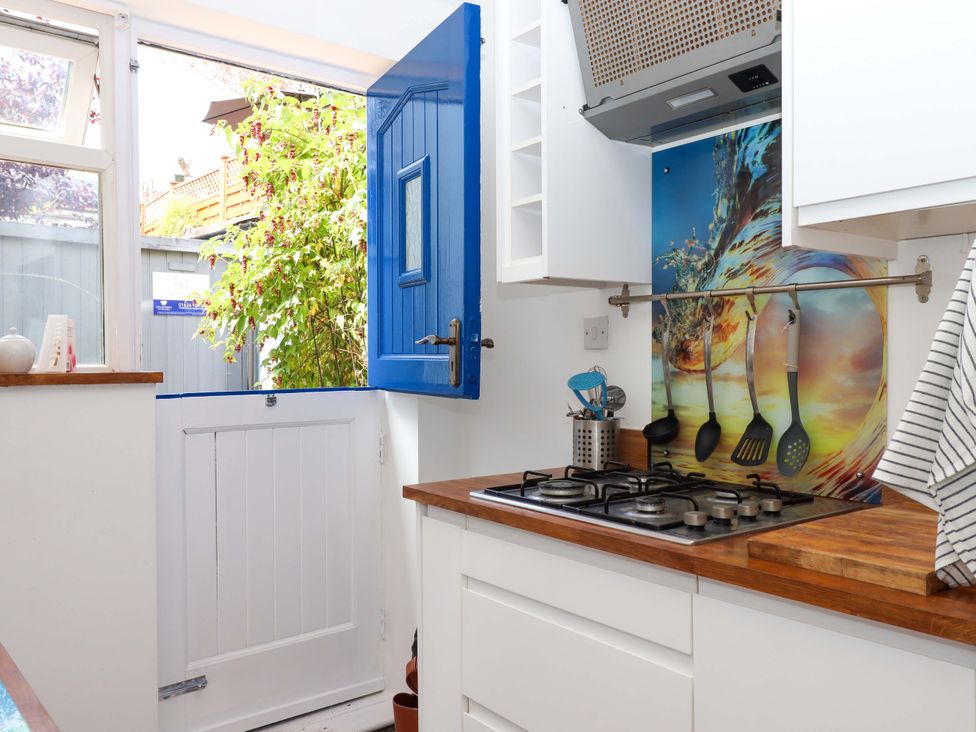 A kitchen with a gas stove and a blue door at Kenny Cottage in Dawlish