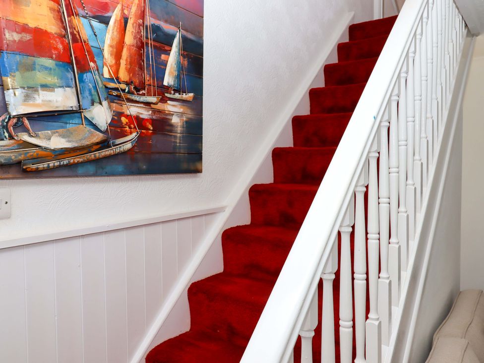 A staircase with red carpet and a painting of boats at Kenny Cottage in Dawlish