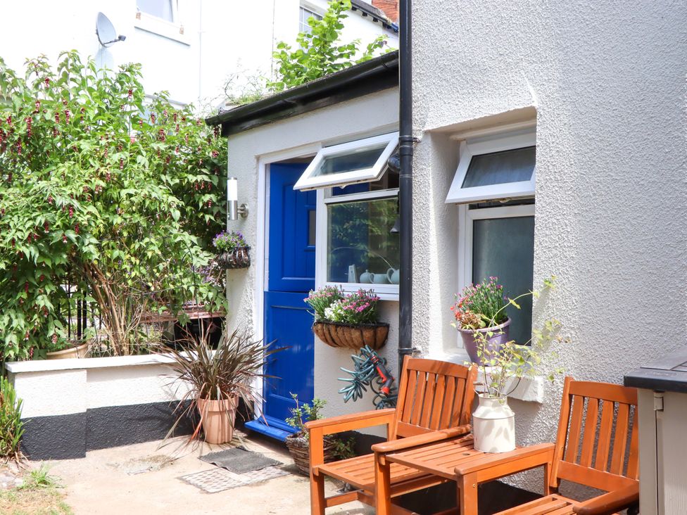 An outdoor area with a blue door, window, plants, and seating at Kenny Cottage in Dawlish