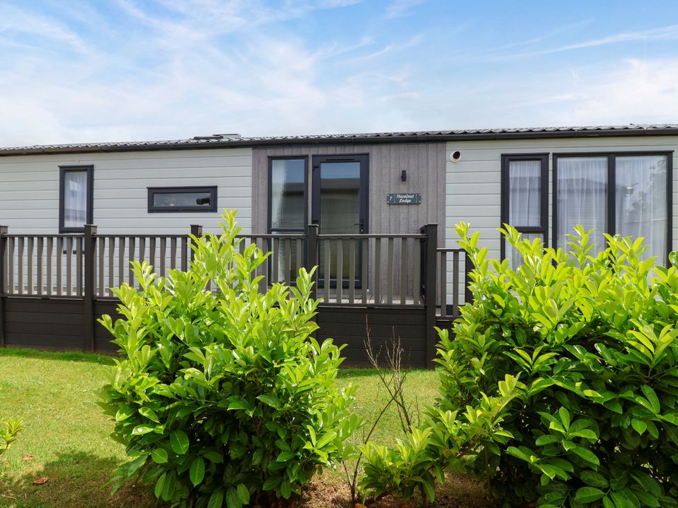 A mobile home with a deck and bushes at Hazelnut Lodge in Chipping Norton