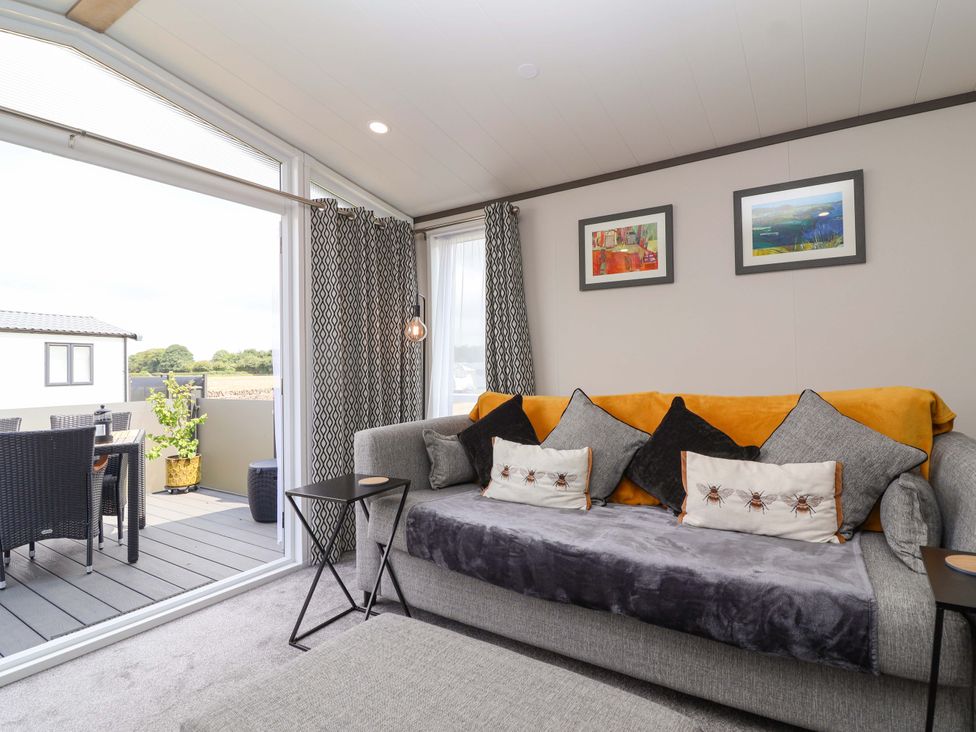 A living room with a sofa and views of outdoor seating at Hazelnut Lodge in Chipping Norton