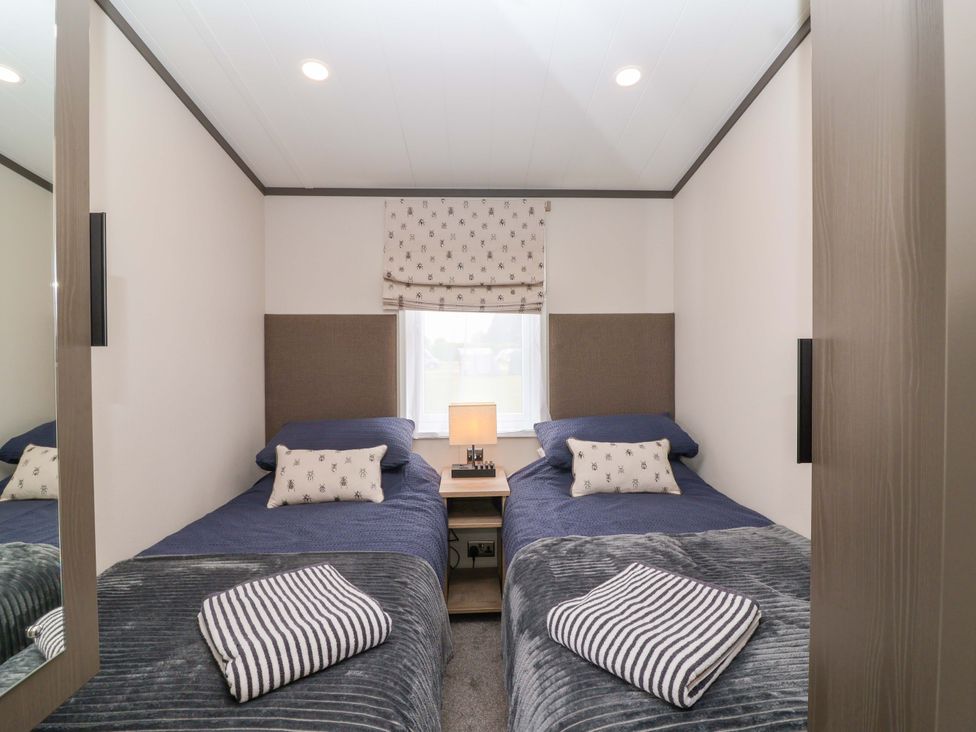A bedroom with two beds and a bedside table at Hazelnut Lodge in Chipping Norton