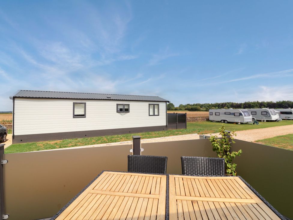 An outdoor area with a table and chairs overlooking caravans at Hazelnut Lodge in Chipping Norton