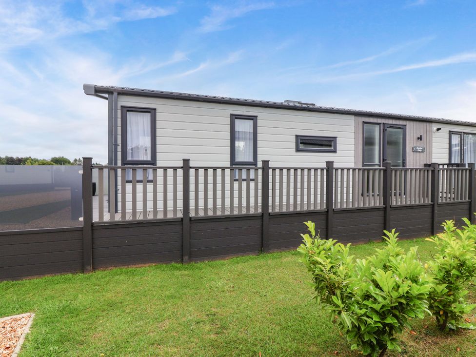 An exterior view of a lodge with a fence in Hazelnut Lodge in Chipping Norton