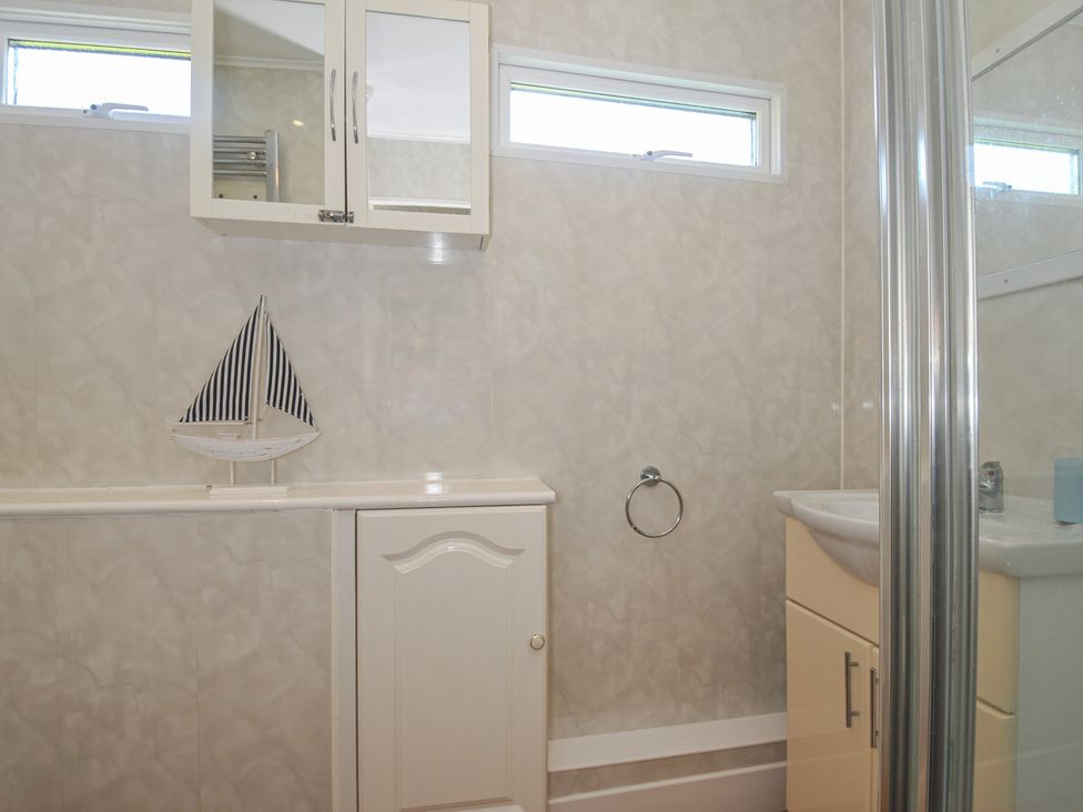 A bathroom with a sink, mirror, and shower at 8 Hillside, Bude