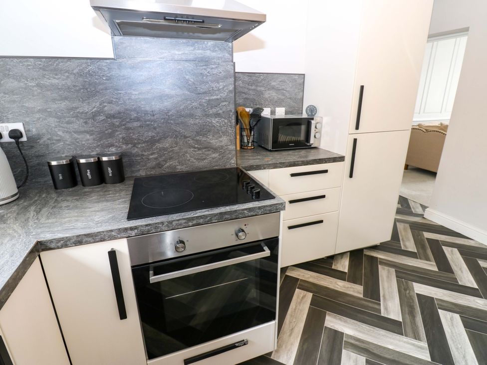 A kitchen with oven, cooktop, microwave, and cabinets at Lowther Suite Whitehaven