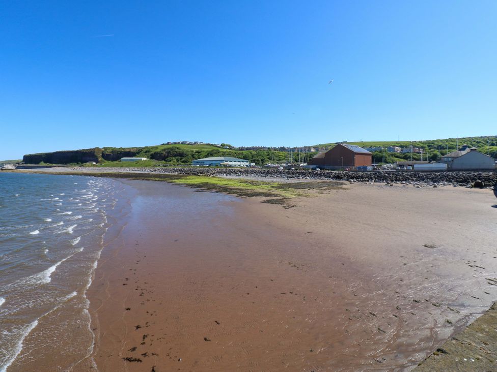 A beach with water and buildings near the shoreline at Lowther Suite in Whitehaven
