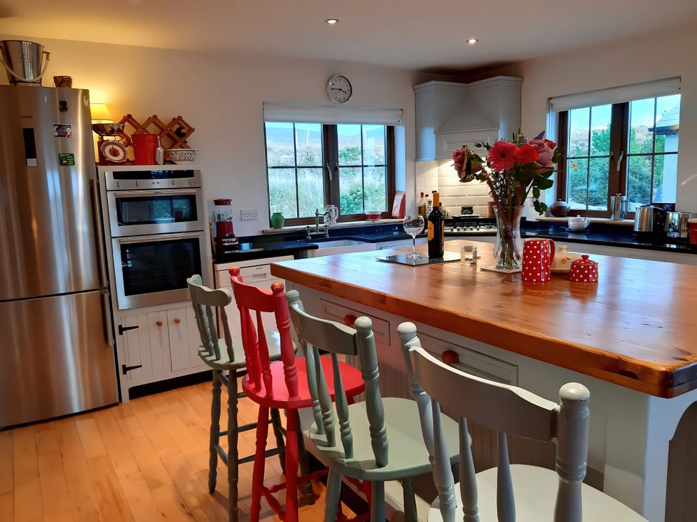 A kitchen with a wooden bar, chairs, flowers, and appliances at Moynish Mor Mulranny in MULRANNY