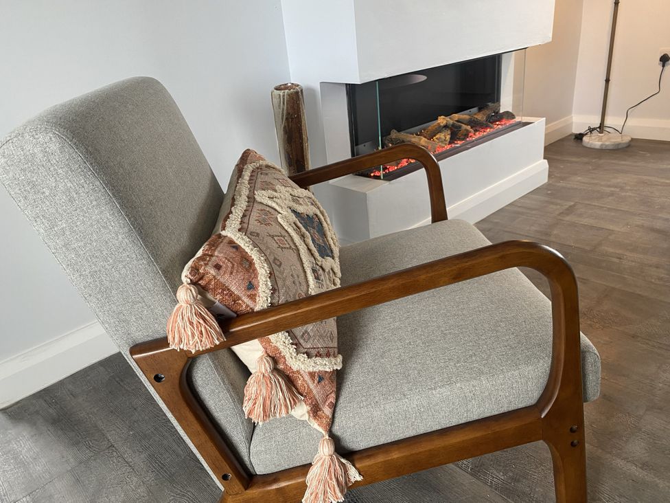 A chair with a cushion next to a fireplace at The Gatekeepers Cottage - Skerry Vore Bryn Pydew near Llandudno Junction