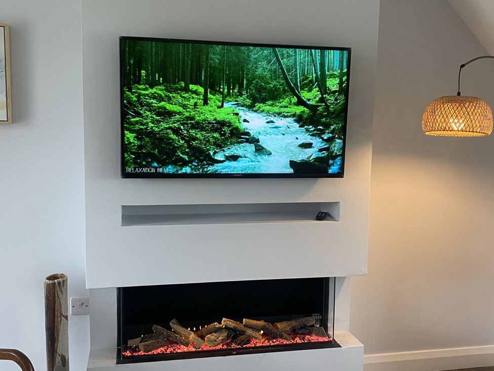 A living room with a television displaying a relaxation film and an electric fireplace at The Gatekeepers Cottage - Skerry Vore, Bryn Pydew near Llandudno Junction