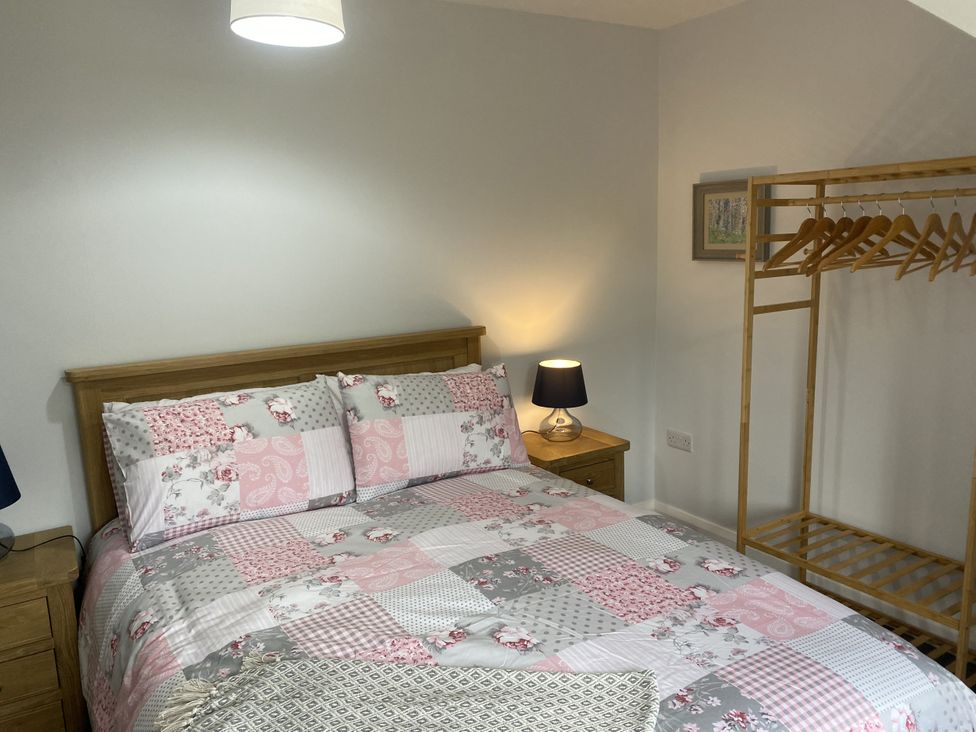 A bedroom with a bed, table, lamp, and clothes rack at The Gatekeepers Cottage - Skerry Vore Bryn Pydew near Llandudno Junction