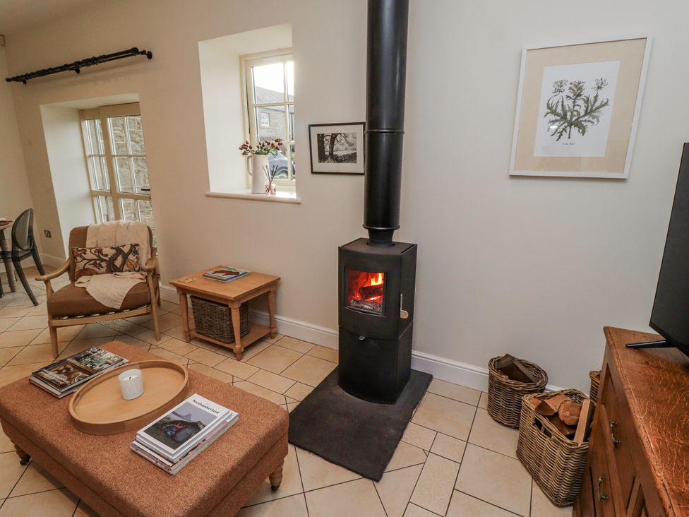 A living room with a stove and seating area at Watermill Cottage in North Charlton