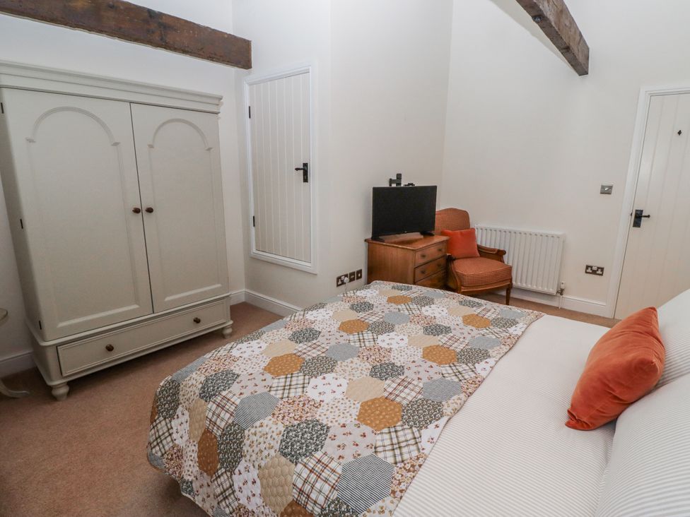 A bedroom with a bed, wardrobe, and TV at Watermill Cottage North Charlton
