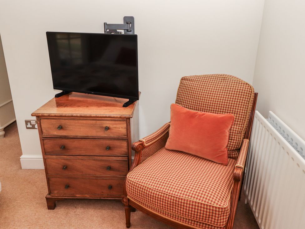 A bedroom with a television on a chest of drawers and an armchair at Watermill Cottage North Charlton