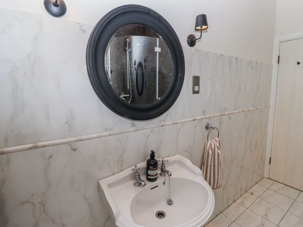 A bathroom with a sink and round mirror at Watermill Cottage in North Charlton