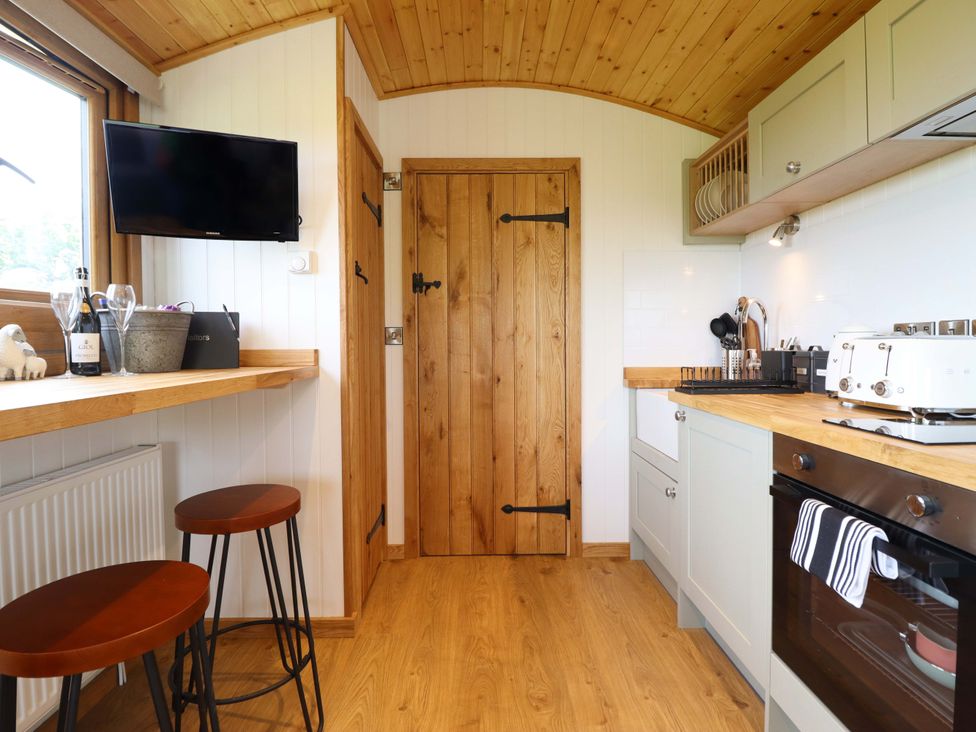 A kitchen with a television, bar stools, and oven at Defaid Cymreig in Oswestry