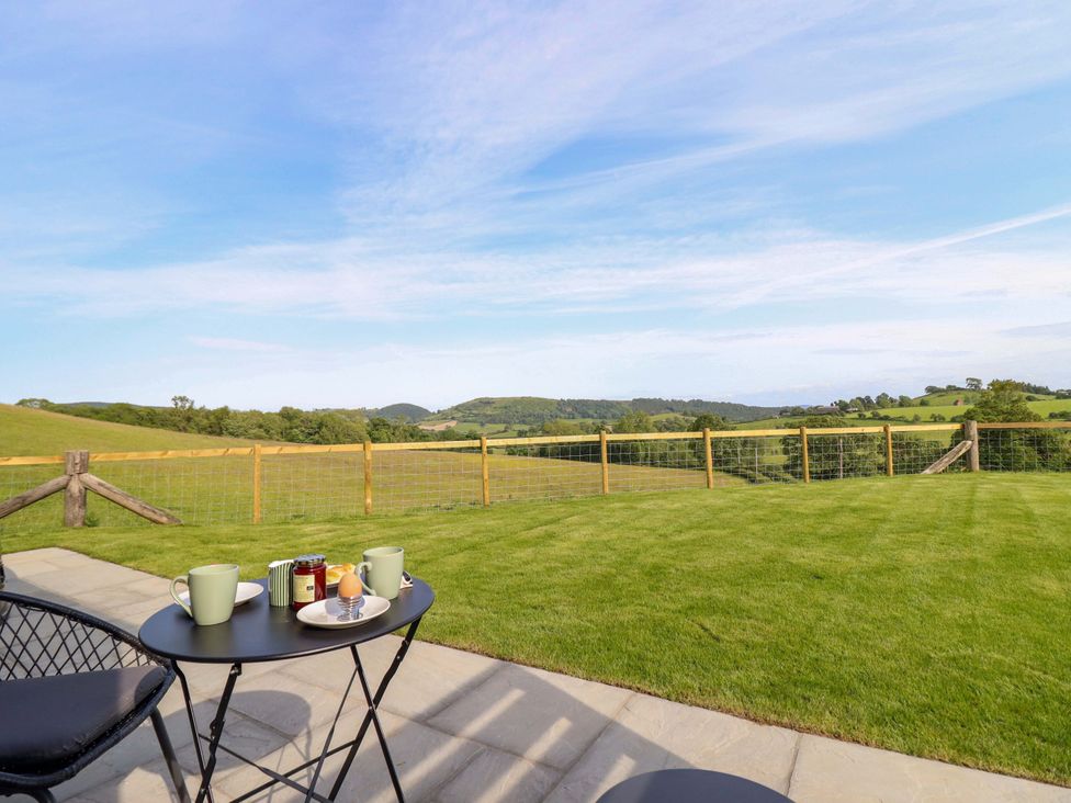 A table with cups and a plate on a patio with a view at Defaid Cymreig in Oswestry