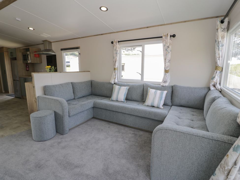 A living room with a sectional sofa and windows at Puffin Way Holiday Caravan