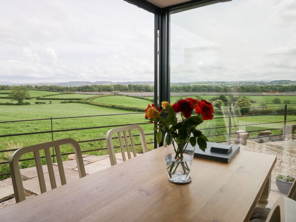 A dining room with a table and flowers overlooking green fields at Lindeth Croft in Carnforth
