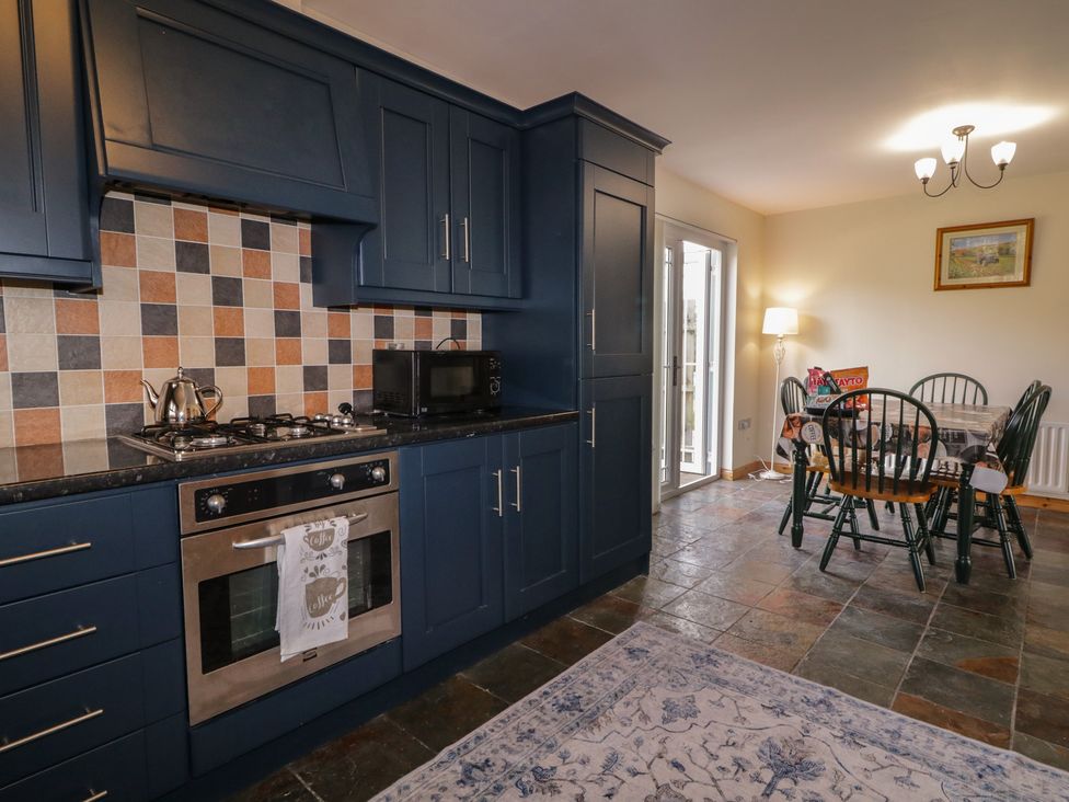 A kitchen with cabinetry, stove, refrigerator, and dining table at The Sperrin Getaway in Omagh