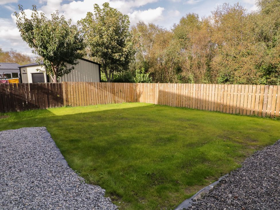 A garden with grass, gravel, fence, and trees at The Sperrin Getaway in Omagh