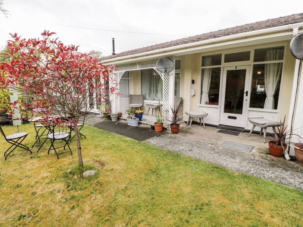A garden with chairs and tables in front of a bungalow at 3 Riverside Bungalows Llanbedr