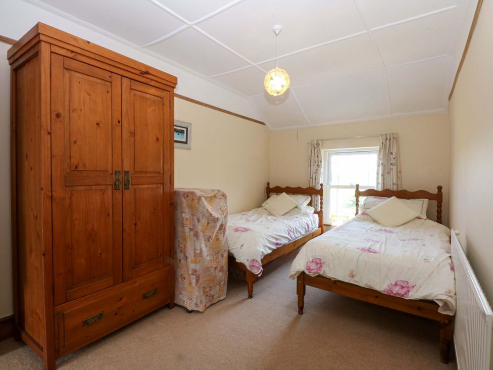 A bedroom with two beds and a wardrobe at Disgwylfa in Sarn Mellteyrn