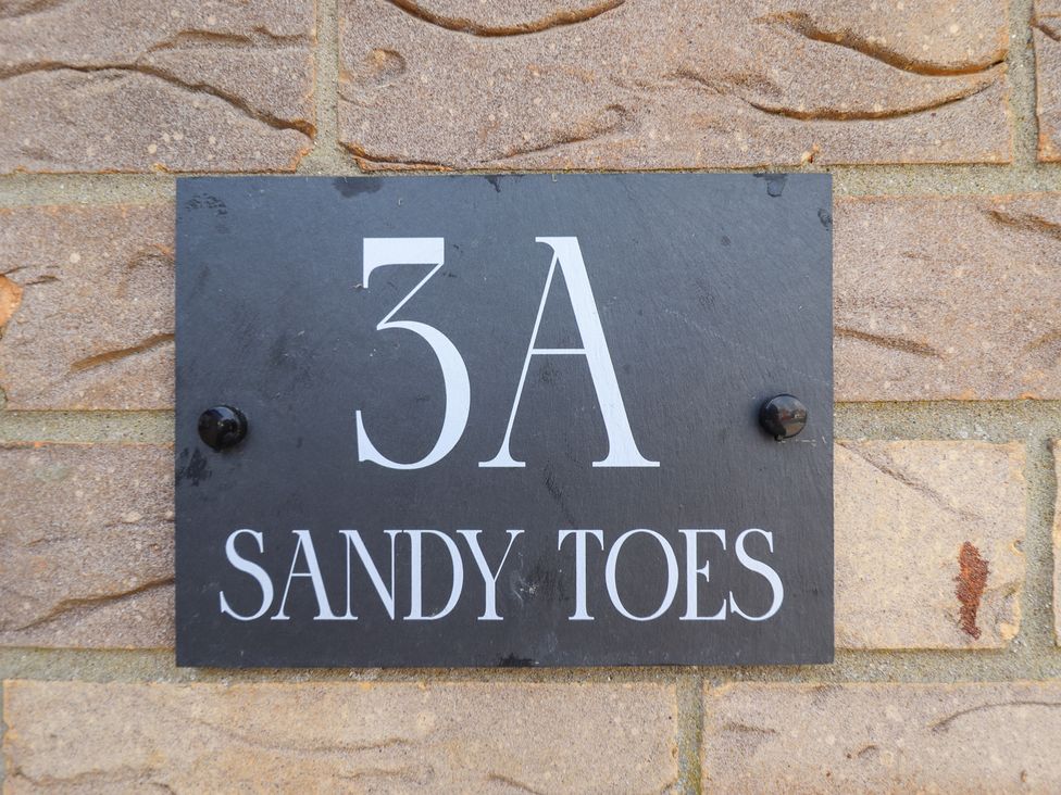 A house number and nameplate on a brick wall at Sandy Toes in Trusthorpe