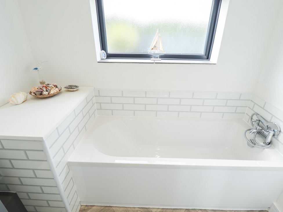 A bathroom with a bathtub and decorative shells at Sandy Toes in Trusthorpe