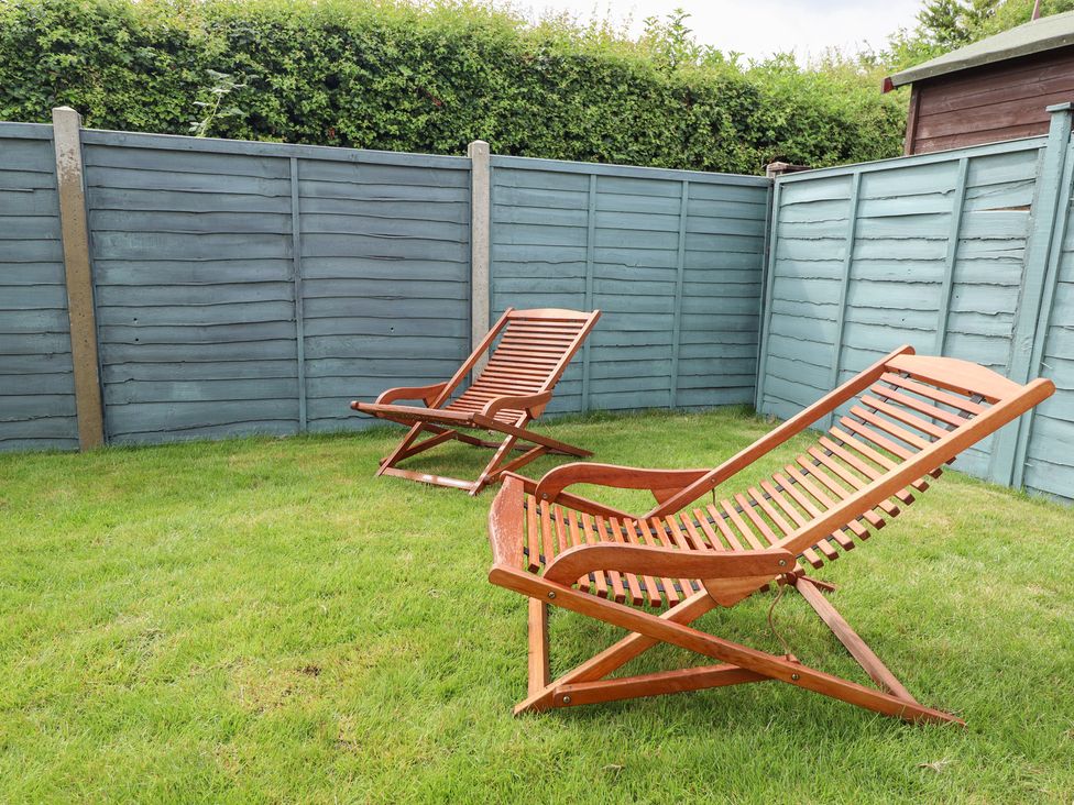 A garden with two deck chairs and a wooden fence at Sandy Toes in Trusthorpe