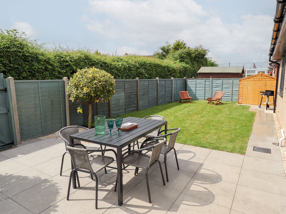 A garden with a table and chairs and green lawn at Sandy Toes in Trusthorpe