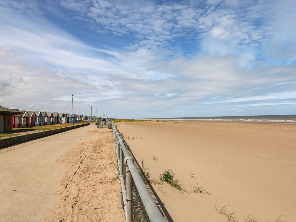 A beach with beach huts and a footpath at Sandy Toes in Sutton-On-Sea