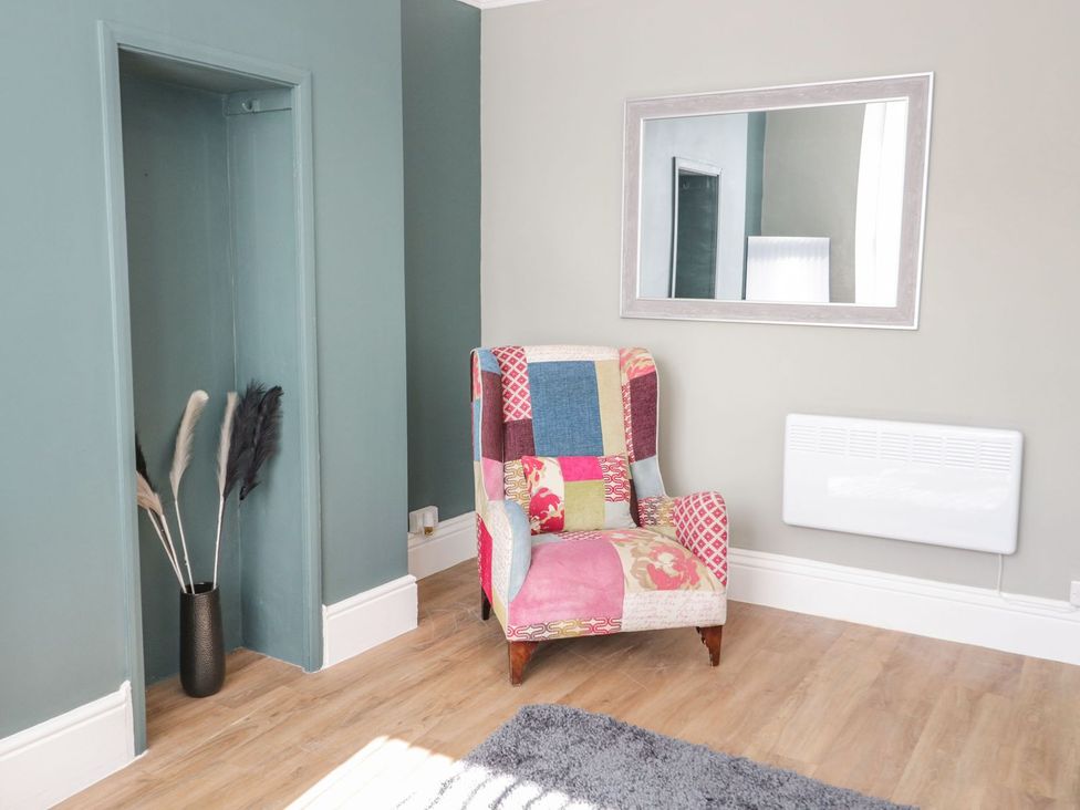 A living room with an armchair and a mirror at Flat 1A, Mona House in Conwy