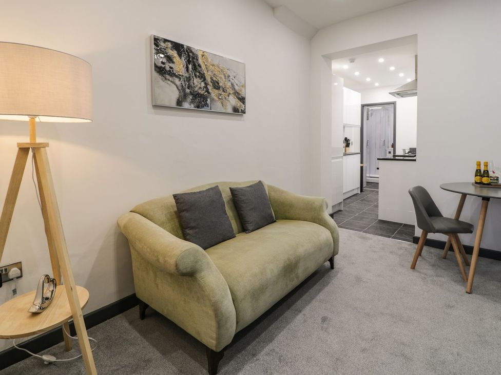 A living room with a sofa, lamp, and kitchenette at Flat 1, Mona House in Conwy