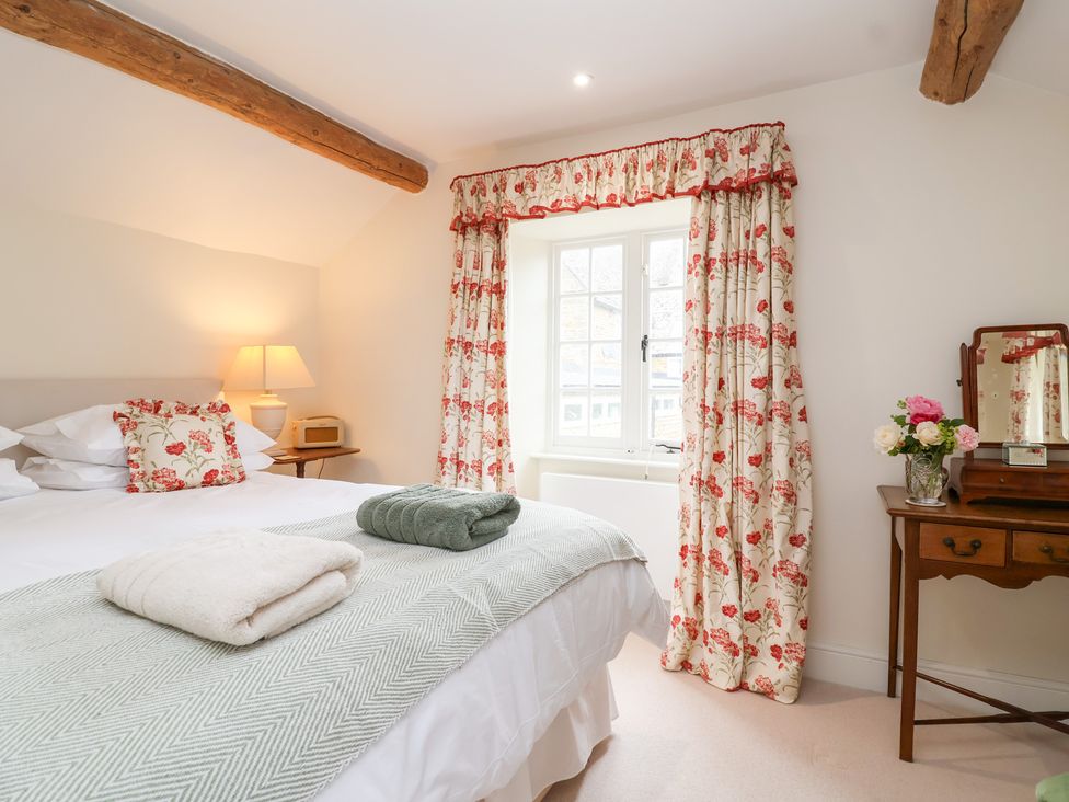A bedroom with a bed and dressing table at Magdalen Cottage in Hook Norton